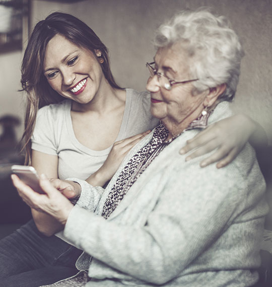 Giovane donna e donna anziana che digita sullo smartphone mentre entrambe guardano lo schermo.