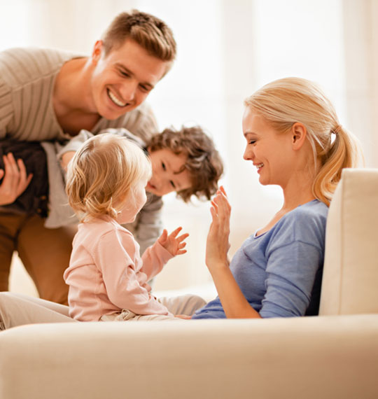 Famiglia seduta sul divano; i bambini sono in braccio ai genitori
